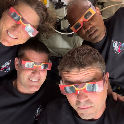 Four people wearing black shirts and eclipse glasses look up at the camera indoors, their excitement echoing the spirit of the Artemis II distance record mission.