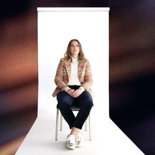 A woman sits on a chair in front of a white backdrop; the blurred profile of a child with a tear rolling down their cheek is visible in the foreground.