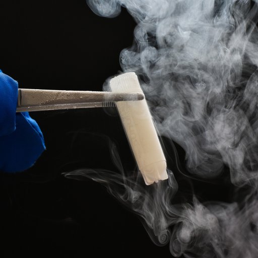 A gloved hand holds a smoking test tube with tongs against a dark background.