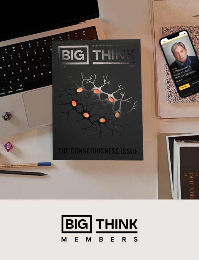 A "Big Think" magazine titled "The Consciousness Issue" on a desk with a laptop, phone, book, notepad, pencil, and dice.