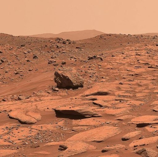 Rocky, reddish Martian landscape with scattered boulders and a hazy sky.