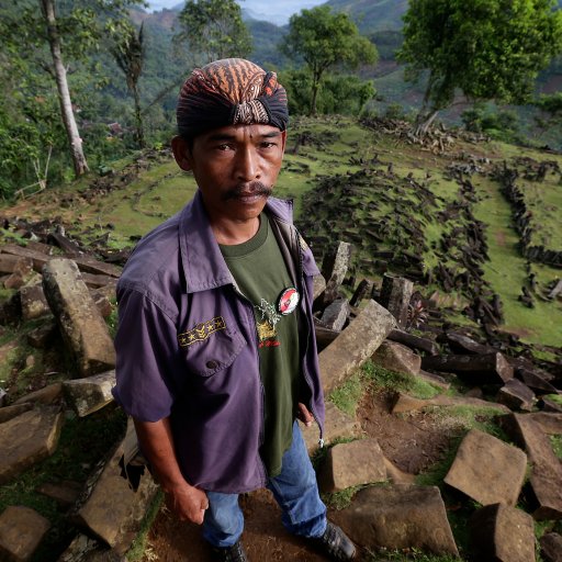 A man standing on top of rocks in the jungle, surrounded by foliage and towering trees.