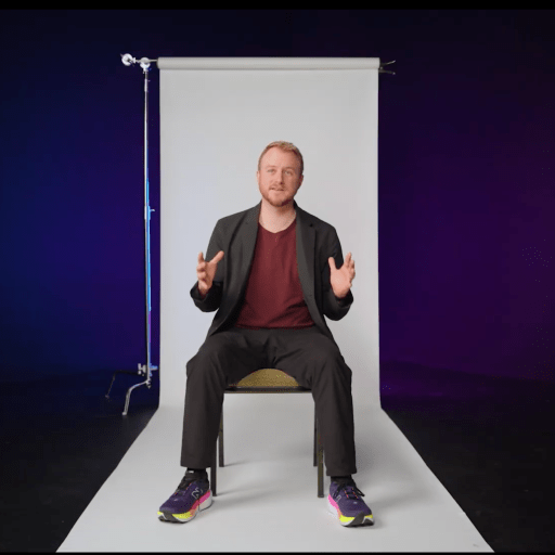 A person sits on a chair in front of a white backdrop, gesturing with both hands. The background fades from dark blue to purple. The BT logo appears in the top right corner.